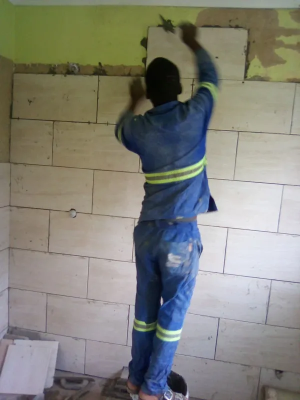 Worker placing overhead wall tiles during a full bathroom remodel