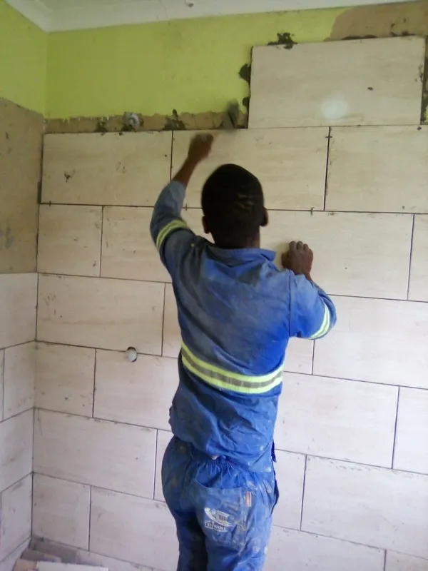 Skilled tiler fitting tiles on upper wall section